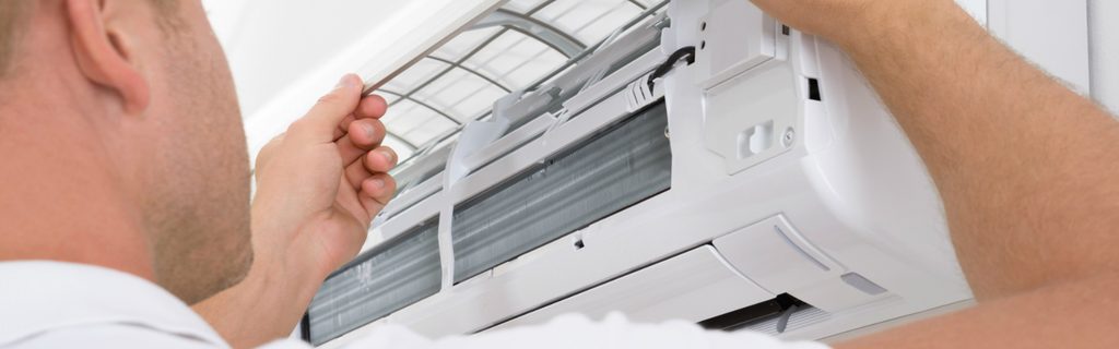 Technician performing maintenance on a white wall-mounted air conditioner, removing the front panel
