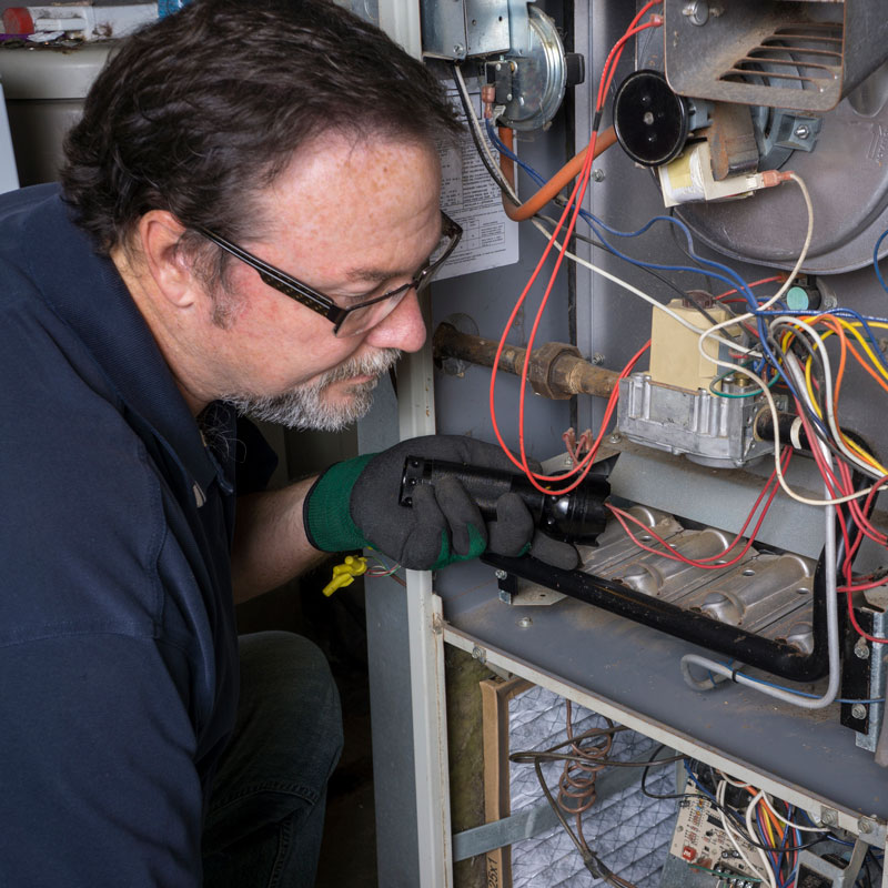 HVAC technician wearing gloves, inspecting wiring inside an open furnace.